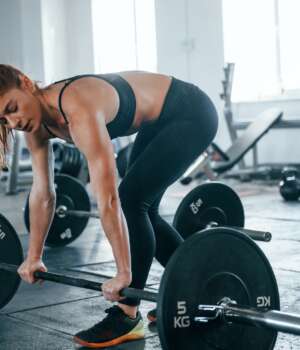 Young fitness woman with slim type of body doing exercises by using barbell