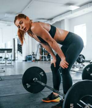 Young fitness woman with slim type of body doing exercises by using barbell